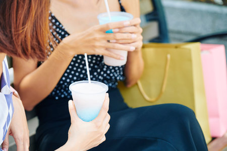 Close-up of woman holding disposable cup of milk cocktail while talking to her friend during their leisure time outdoorsの写真素材