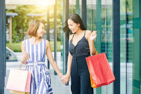 Happy Asian girls with paper shopping bags holding hands and happy with their purchases while walking in the cityの写真素材
