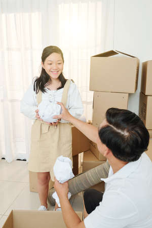 Happy Vietnamese girl giving wrapped vase to her father packing cardboard boxesの写真素材