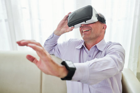 Happy emotional man wearing virtual reality goggles when playing videogame at home