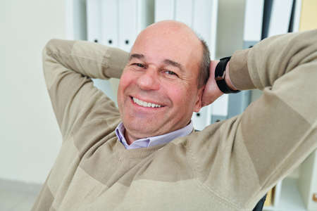 Happy mature businessman leaning back in his armchair and enjoying short break after day of workの写真素材