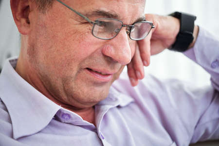 Face of middle-aged experienced entrepreneur in glasses smiling when reading information on gadget screenの写真素材