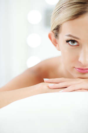 Half face of beautiful young woman with flawless nude make-up leaning on her hands and looking at cameraの写真素材