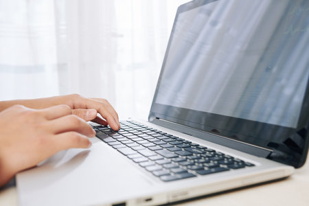 Hands of teenage boy searching information for school on the internet via laptop