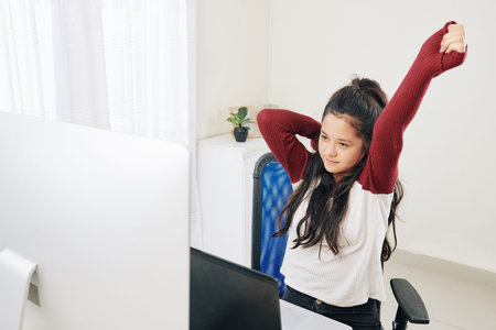 Stretching tired teenage girl looking at programming code on screen of computer