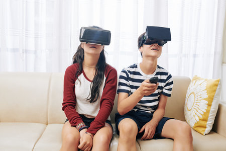 Teenage boy using remote control to switch programs in virtual reality heasets for him and his...