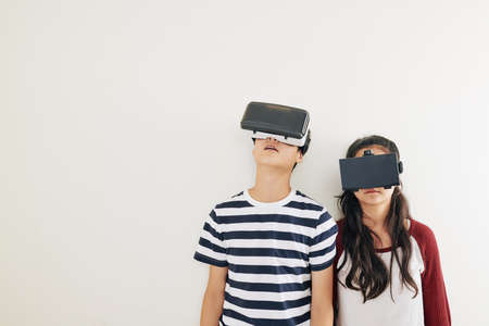 Children in casual clothes wearing virtual reality glases when standing against white wallの写真素材
