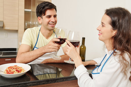 Young smiling Caucasian couple drinking red wine before eating dinner at home