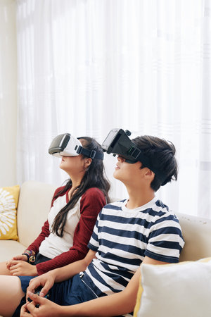 Curious teenager sitting on sofa and watching movie in virtual reality glasses