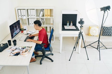Creative young Vietnamese freelance designer working on computer at table in his home studio