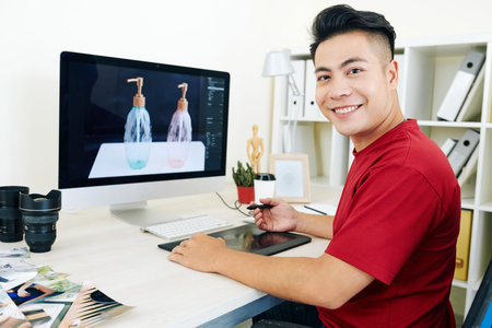 Cheerful young Vietnamese professional 3D designer working on graphic tablet on visualization for...