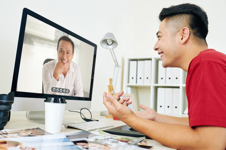 Smiling creative young man video calling his coworker or boss to discussing project details