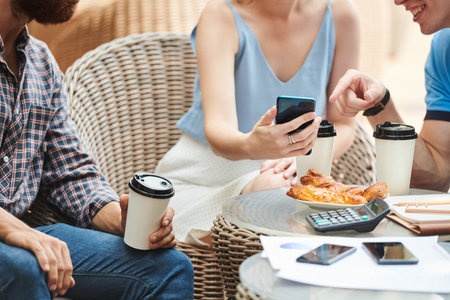 Group of coworkers enjoying coffee break in cafeteria and discussing funny picture on screen of...