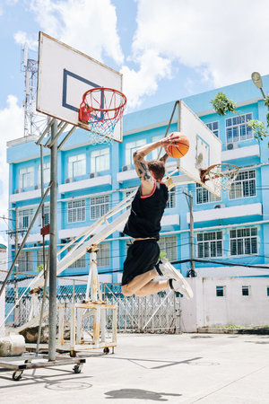 Basketball player in uniform jumping high to throw ball in basket when he is playing on street court