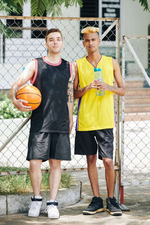 Full-length portrait of serious young handsome guys playing game of basketball on street courtの写真素材