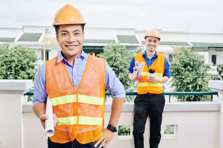 Multi-ethnic team of smiling construction workers standing outdoors with scrolls of blueprints and building plansの写真素材
