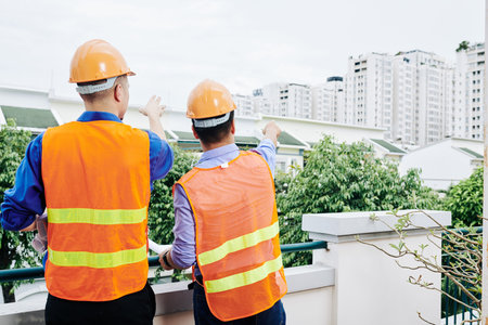 Rear view of civil engineers in bright orange vests pointing at building in new district they were designingの写真素材