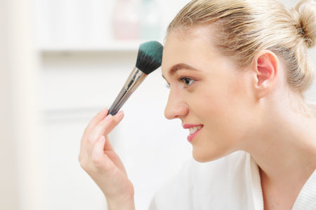 Smiling pretty young woman applying matte face powder to fix make-up