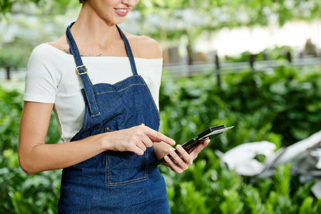 Cropped image of nursery garden manager using nfs device attached to smartphone when entering sum of...