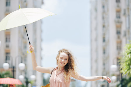 Happy young pretty woman walking in the street with umbrella in hand on windy dayの写真素材