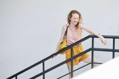 Happy laughing pretty girl leaning on railing and looking down from the staircaseの写真素材