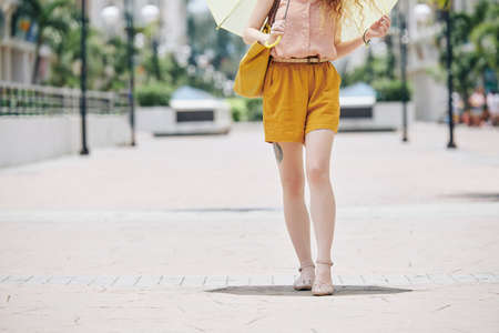 Cropped image of young woman walking on pavement with umbrella on sunny dayの写真素材