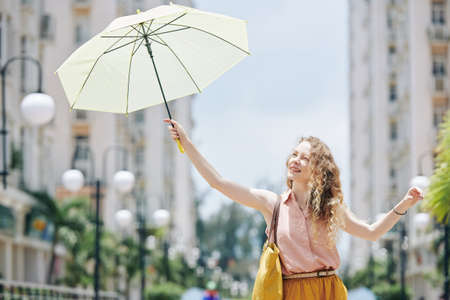Pretty curly young woman using umbrella to protect herself from shining sunの写真素材