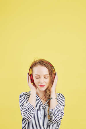 Beautiful young woman closing her eyes and enjoying listening to meditation and ambient sounds via application to manage stress and calm anxietyの写真素材
