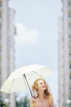 Beautiful young Caucasian woman with big white umbrella walking in cityの写真素材