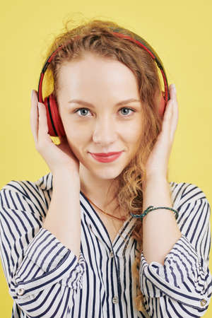 Portrait of pretty smiling young woman in striped blouse enjoying listening to podcast in headphonesの写真素材