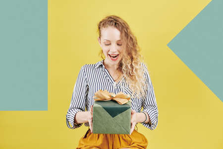 Excited young pretty woman looking at present wrapped in green paper with big golden bowの写真素材