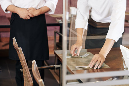 Close-up of waiter serving the table he putting knives and forks on the table with manager standing near by at the restaurantの写真素材