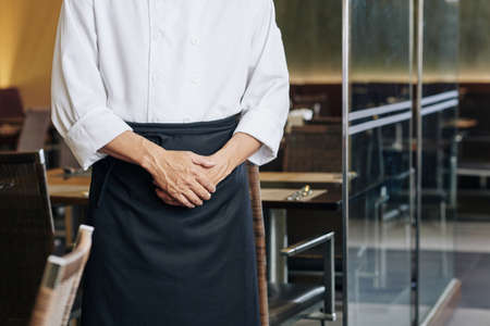 Close-up of male waiter in apron standing at the restaurant and meeting the guestsの写真素材