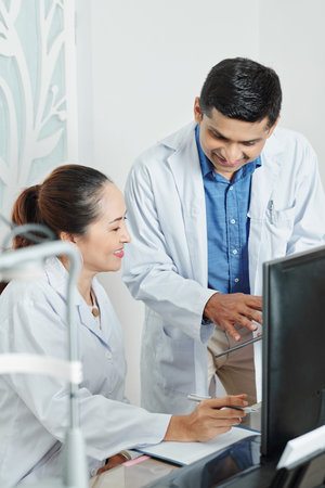 Multiethnic couple of doctors discussing some disease together using digital tablet at office