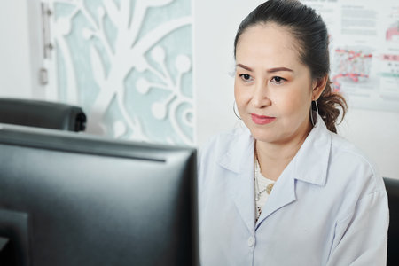 Asian mature female woman looking at computer monitor while working at her workplace at office