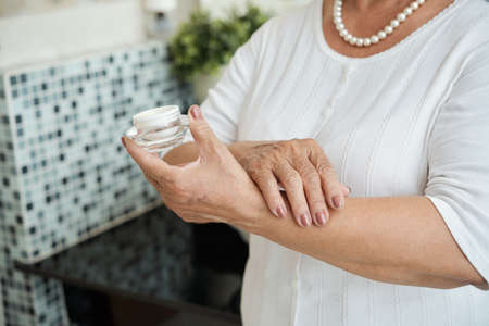 Close-up of senior woman holding moisturier and applying it on her handの写真素材