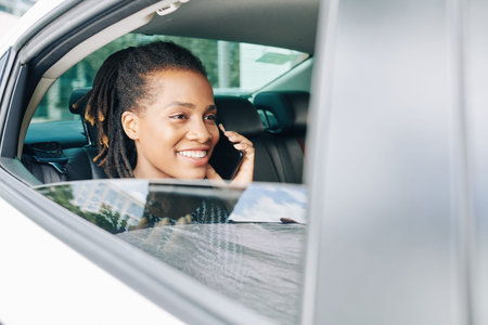 Happy African woman sitting on back seat as a passenger and talking on mobile phone in car