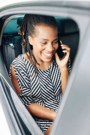 Young African woman sitting on back seat and talking on mobile phone while trip by car
