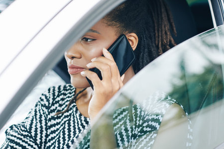 African serious woman watching the road and talking on mobile phone while driving her car