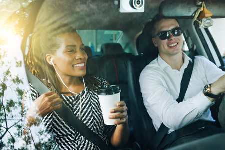 African young woman drinking coffee smiling and talking to young man while he driving a car