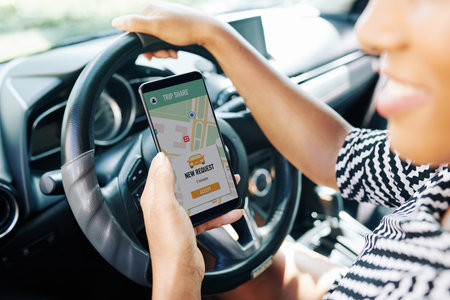 Close-up of female driver sitting behind the wheel and using her mobile phone she looking for the companions in online applicationの写真素材