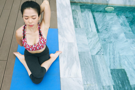 Asian healthy woman sitting on exercise mat with her eyes closed and stretching during yoga outdoors