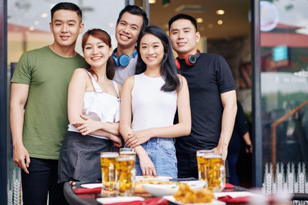 Portrait of Asian young friends smiling at camera while standing together near the table with food...