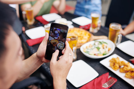 Close-up of young man holding mobile phone and making a photo of meal on the table at the restaurant