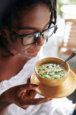 African beautiful woman in eyeglasses holding bowl with exotic food and tasting itの写真素材