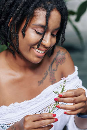 African beautiful woman with beautiful hairstyle holding flower in her hand and smiling outdoorsの写真素材