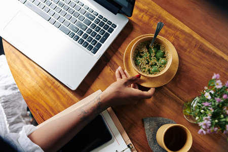 Close-up of young woman sitting at the wooden table with laptop and she is going to eat her dinner