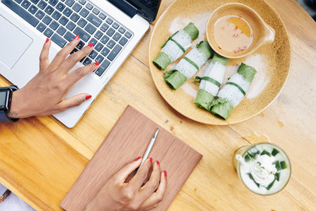 Close-up of businesswoman typing on laptop computer and have dinner at wooden table