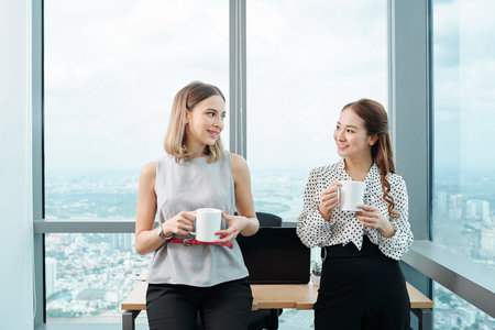 Young positive multi-ethnic female colleagues drinking coffee and discussing latest news during...