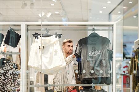 Handsome young man choosing fashionable clothes in fashion boutique in city mall